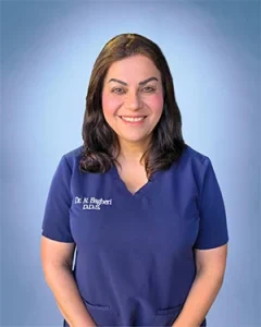 Dr. Bagheri DDS in navy scrubs smiling against blue gradient background.